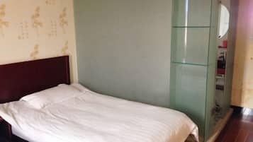 Una cama individual con ropa de cama blanca en una habitación con pared verde y cabecera de madera.