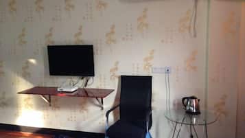 Una habitación con televisión de pantalla plana sobre un soporte, una silla negra, una mesita de cristal con un hervidor y papel tapiz estampado.