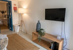 A living room with a television mounted on the wall, a floor lamp, a wooden console table, and a small plant. - Charming 1BD Flat in Lisbon w/Private Entrance (Lisbon)
