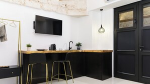 Una cocina moderna con encimera negra, taburetes dorados, un lavamanos negro y un televisor montado en la pared.