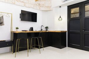 A modern kitchen with a black countertop, gold bar stools, a black sink, and a TV mounted on the wall.