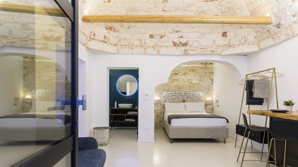 Un dormitorio moderno con cama tipo loft, un escritorio con sillas, un espejo redondo y una pared de piedra.