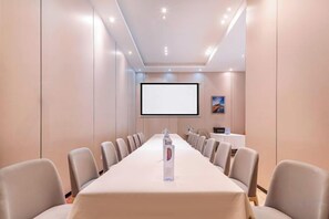 Une salle de conférence équipée d’une longue table, de chaises, d’un écran de projection et d’une bouteille d’eau.