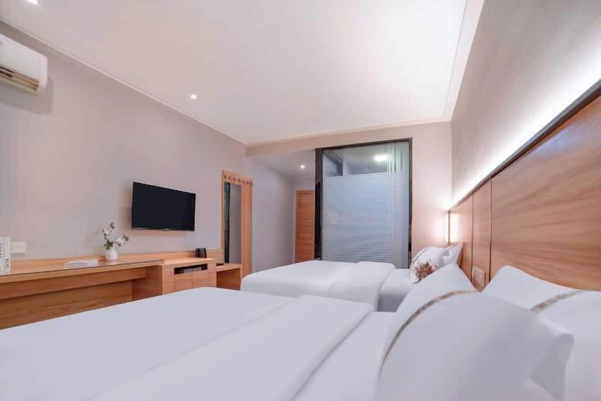 A hotel room with a flat-screen TV, two beds, a wooden desk, and a large window.