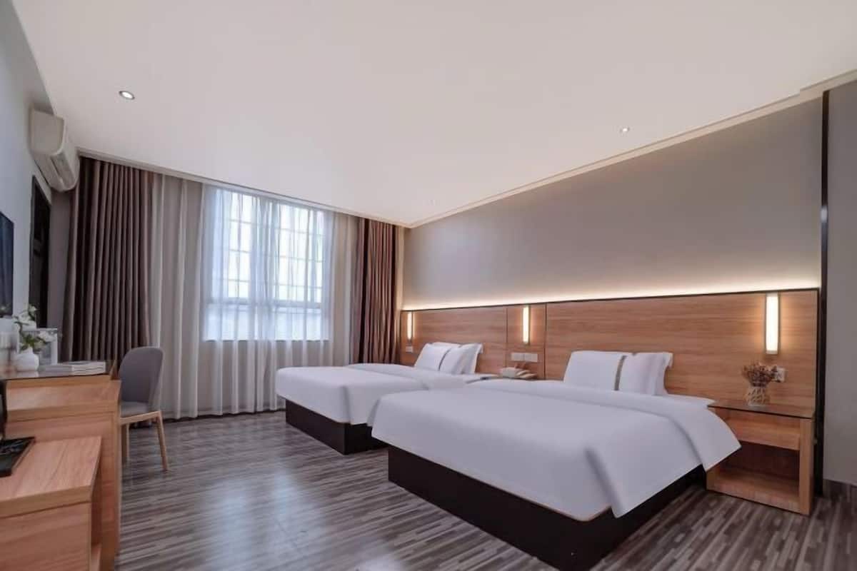 A modern hotel room with two beds, a desk, a chair, and a large window with curtains.