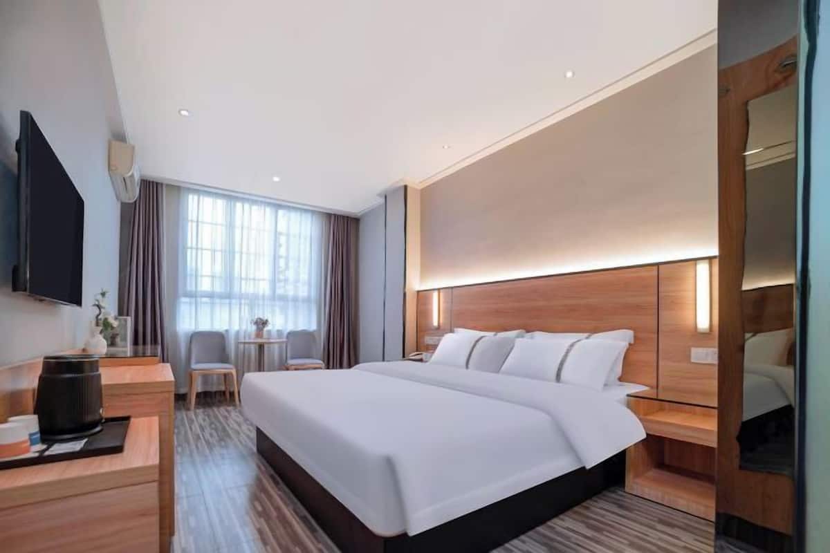 A hotel room with a large bed, a desk with a coffee maker, a TV, and a window with curtains.