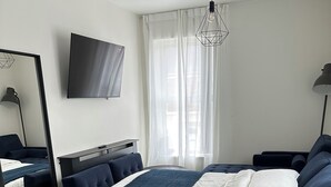 A modern hotel room with a bed, a desk, and a dining area.