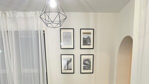 A dining area with a round table, black chairs, and a geometric-patterned table runner. There are framed pictures on the wall and a geometric pendant light above the table.