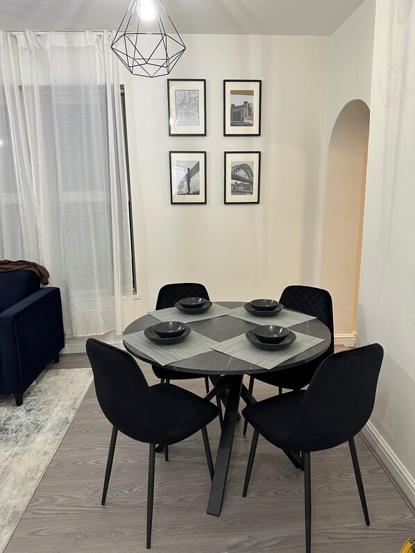 A dining area with a round table, black chairs, and a geometric-patterned table runner. There are framed pictures on the wall and a geometric pendant light above the table. - Modern Apartment, 1km from city!  (Newcastle upon Tyne)