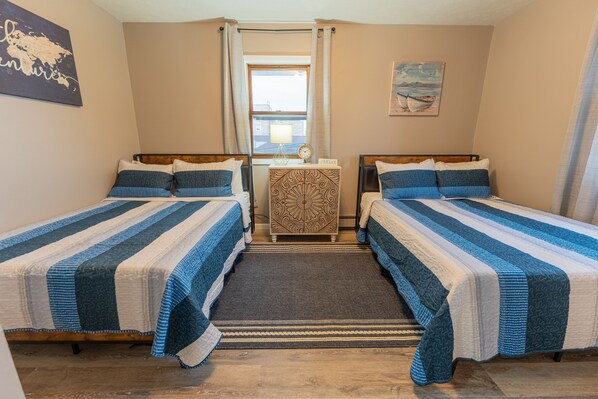 A room with two single beds, a small table with a lamp, and a window with curtains. - Lake Views, Cozy 2-bedroom condo newly remodeled, downtown Escanaba (Escanaba)