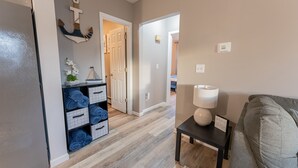 Ein Flur mit Holzboden, einem grauen Sofa, einem kleinen Tisch mit Lampe und einer Tür zu einem anderen Raum.