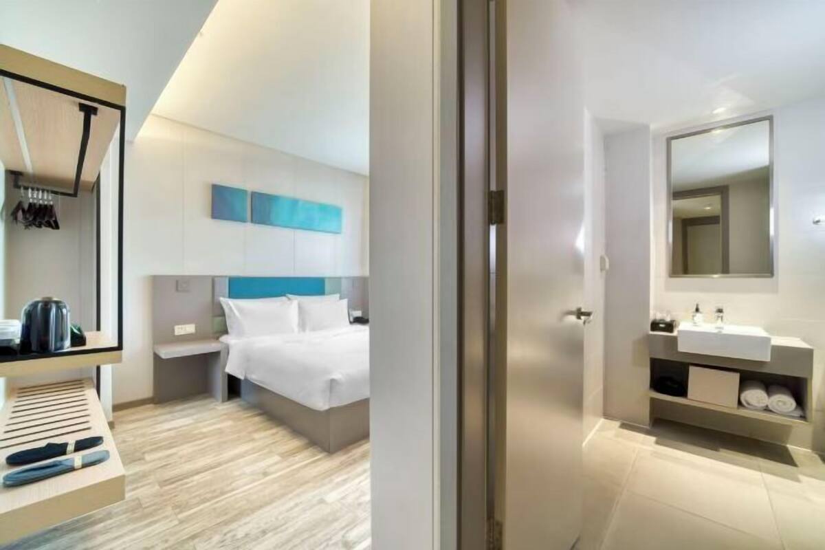 Una camera d'hotel moderna con un letto, comodini e un bagno con lavandino e specchio.