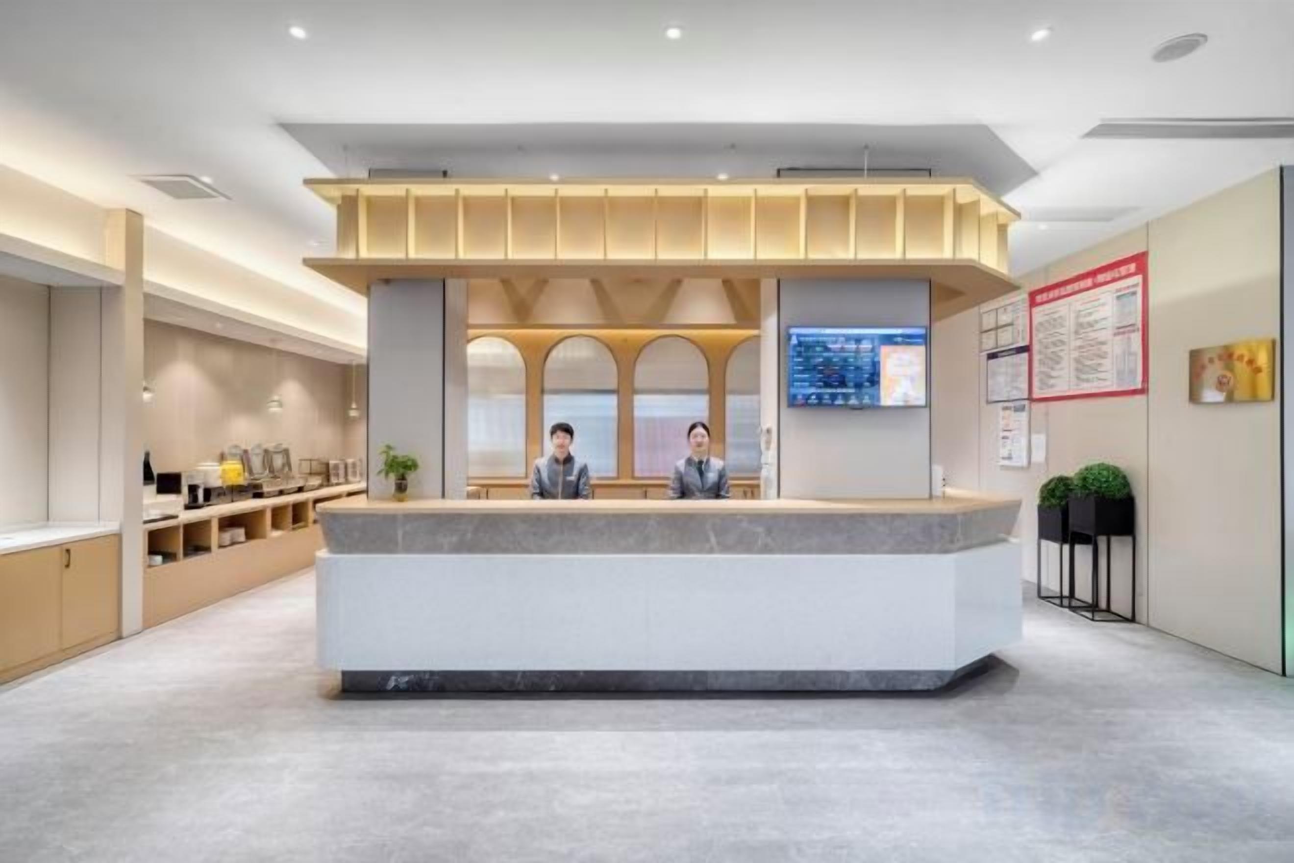 A reception area with a counter, two receptionists, a digital display, and a bulletin board.