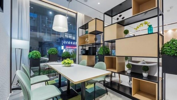 Une salle de réunion moderne avec une table blanche, des chaises vertes et des étagères noires.