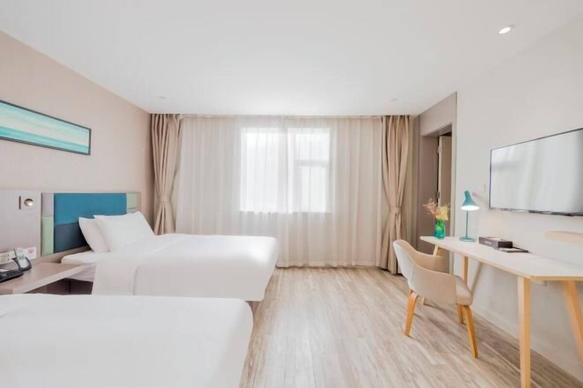 Una camera d'albergo con due letti, una scrivania, una sedia, una TV e una finestra con tende.