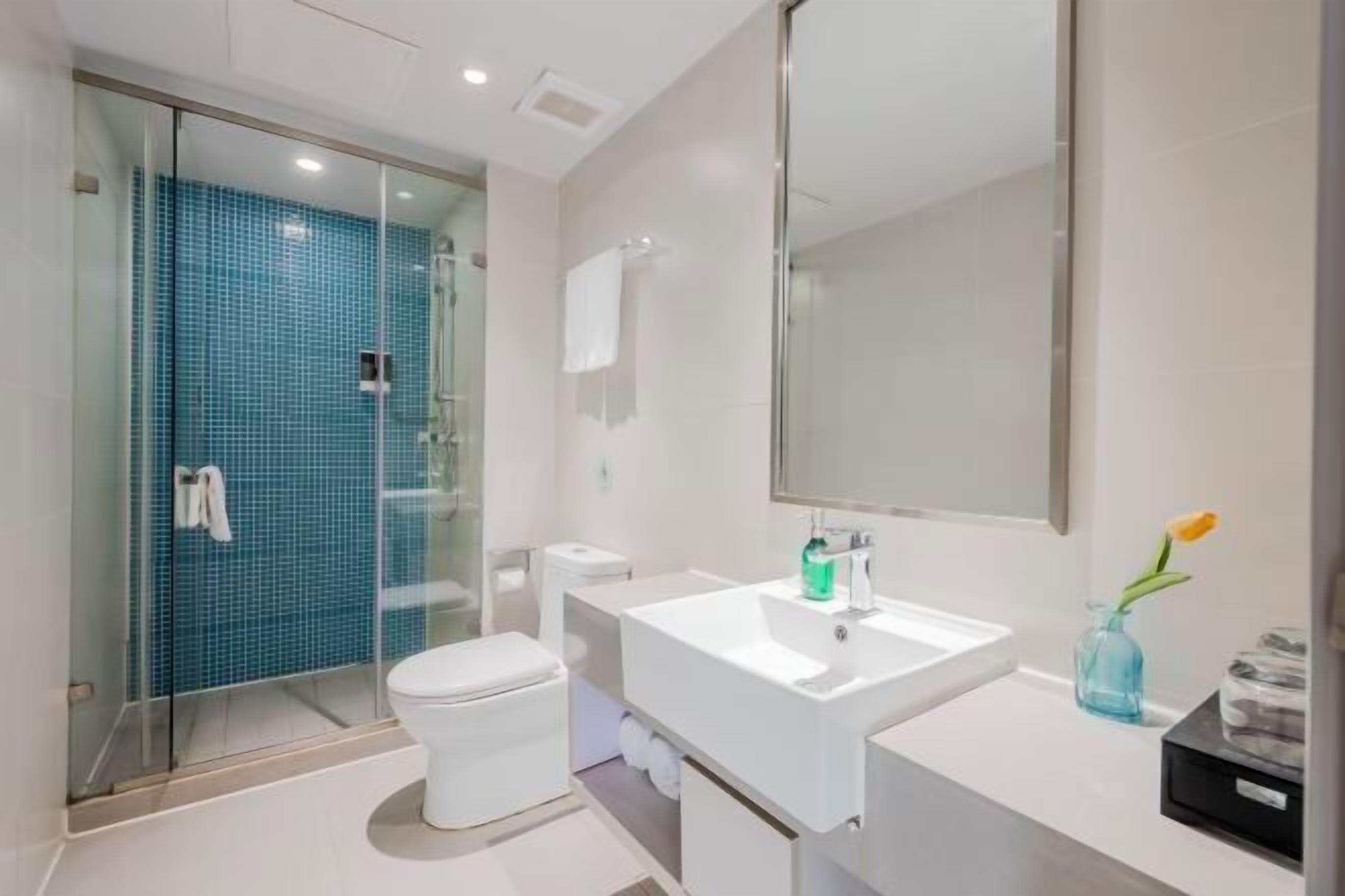 A modern bathroom with a glass shower enclosure, a white toilet, a white sink with a mirror, and a vase with a flower.