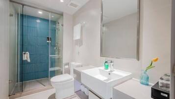 A modern bathroom with a glass shower enclosure, a white toilet, a white sink with a mirror, and a vase with a flower.