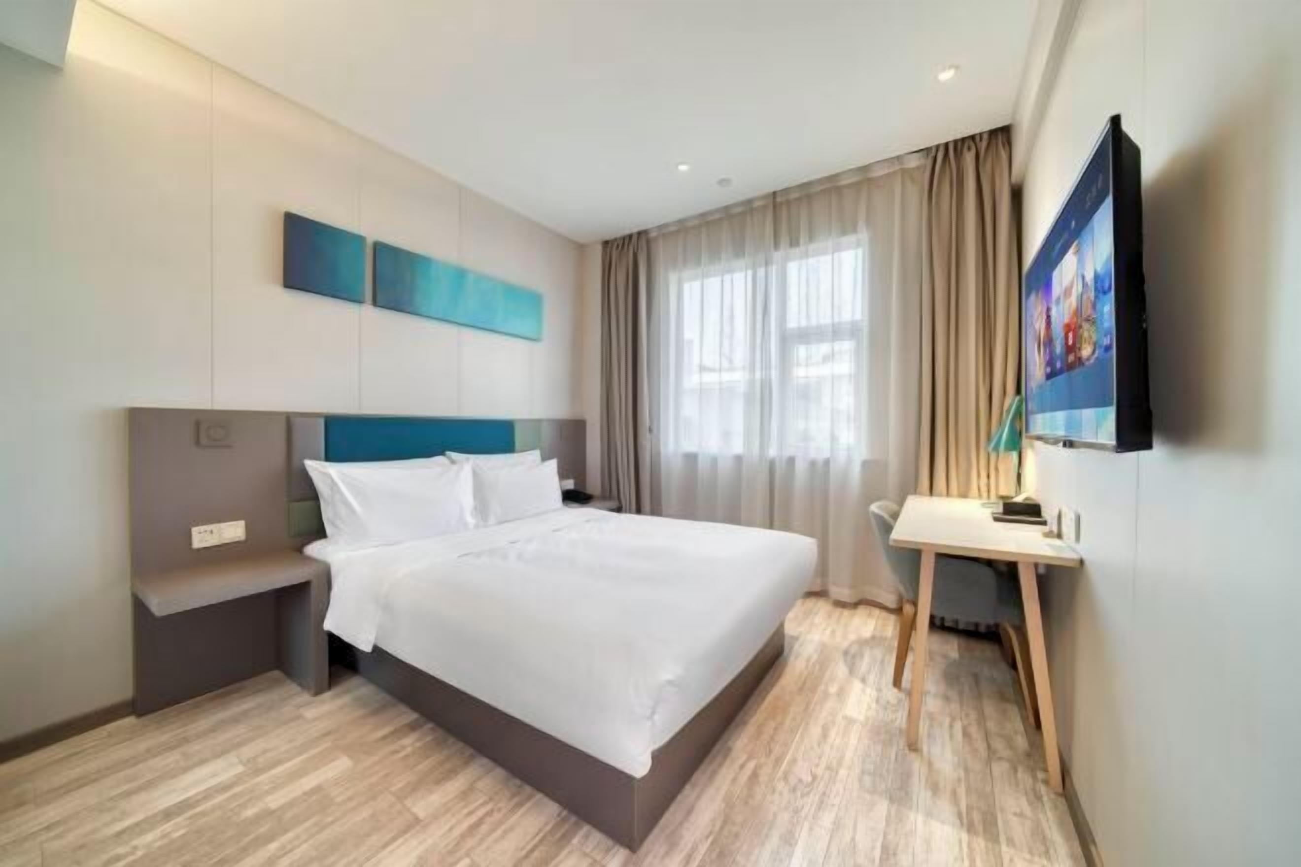 A modern hotel room with a large bed, a desk, a flat-screen TV, and a window with curtains.