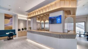 Un espace d’accueil moderne doté d’un comptoir en marbre, d’un écran numérique et d’un coin salon avec un banc bleu.