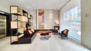 Un espace de détente moderne comprenant un canapé, des fauteuils et une table basse. On y trouve des étagères ornées d’objets décoratifs et une grande fenêtre offrant une vue panoramique.