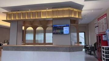 A reception desk with a digital screen, a counter, and a seating area with tables and chairs.