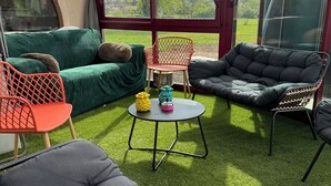 A sunroom with a green couch, two chairs, a small table, and a large window. - Grande Maison à la Campagne aux Portes du Morvan (Fours)