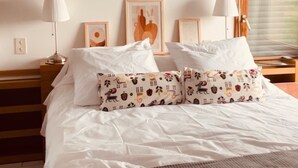 A neatly made bed with white linens and patterned pillows, a wooden nightstand with a lamp, and framed artwork on the wall. - Grande Maison à la Campagne aux Portes du Morvan (Fours)