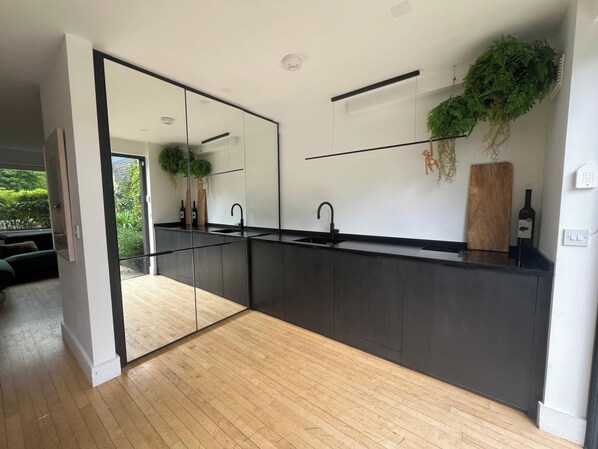 A modern kitchen with a large mirror, dark cabinetry, and a wooden floor.