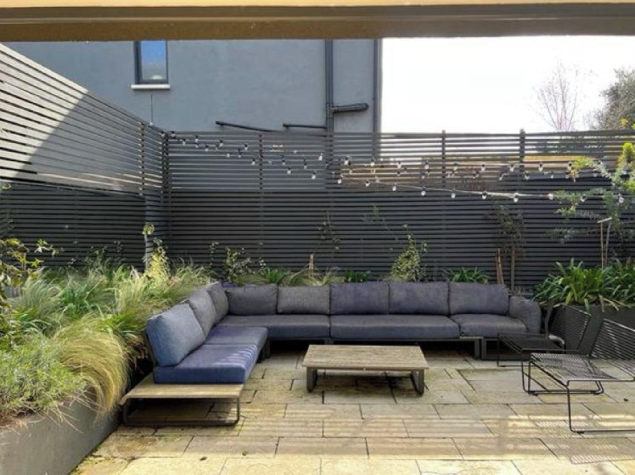 A modern outdoor seating area with a sectional sofa, a wooden table, and a metal bench.