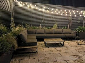 An outdoor seating area with a dark-colored sofa, a small table, and string lights. - Sunlit, Designer Haven in Trendy Neighbourhood (Dublin)
