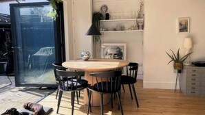 Un espace repas moderne avec une table ronde et des chaises noires, une plante suspendue et une vue à travers une porte vitrée.