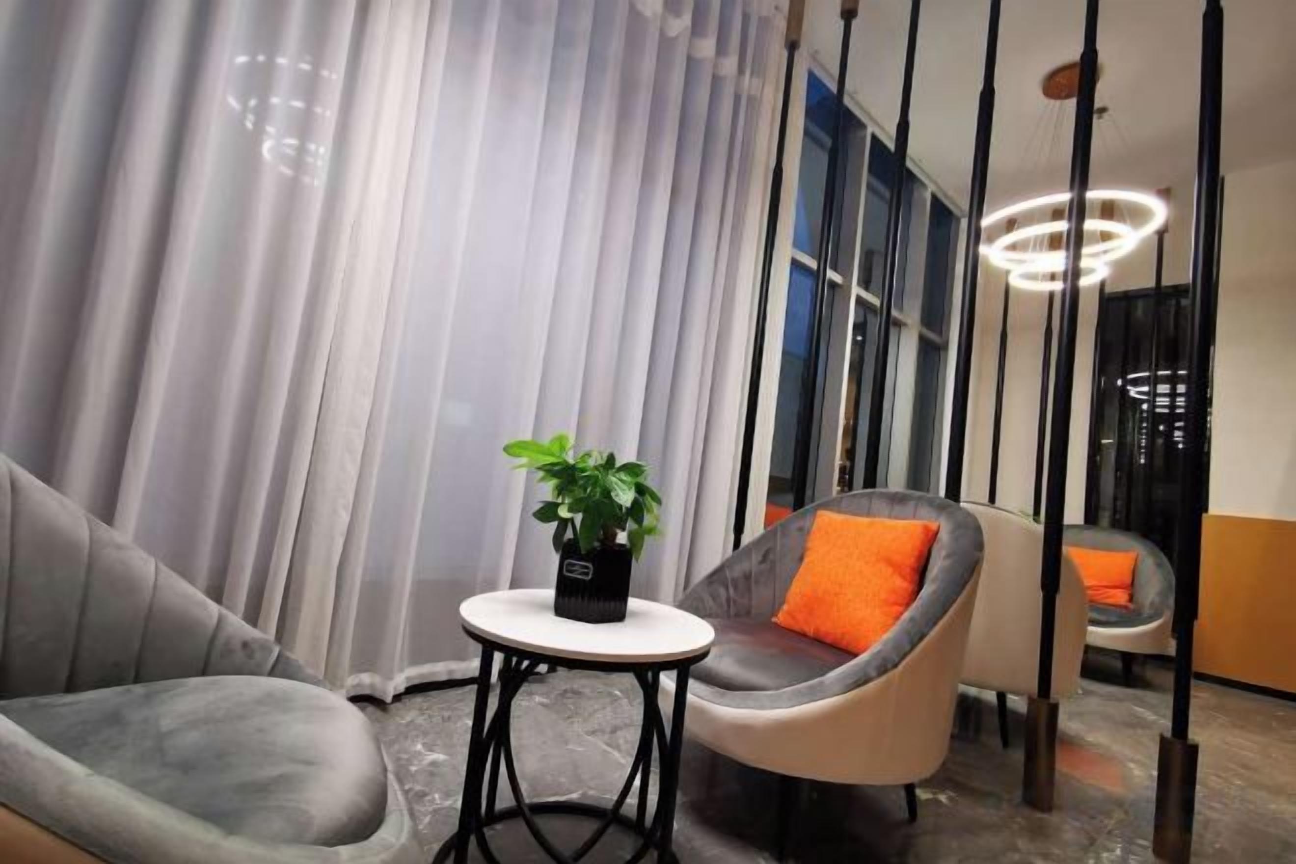 Una habitación moderna con un sofá gris, una mesita redonda con una planta y un sillón gris con un cojín naranja.