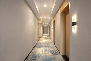 Un passadís d'hotel amb una catifa estampada, il·luminació empotrada i un cartell al mur.