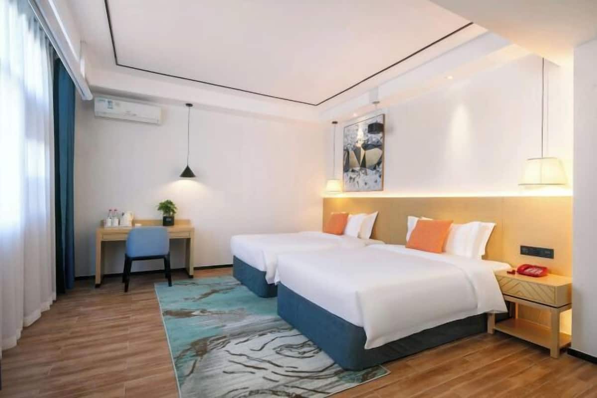 A hotel room with two beds, a desk, a chair, a rug, and a nightstand with a lamp.