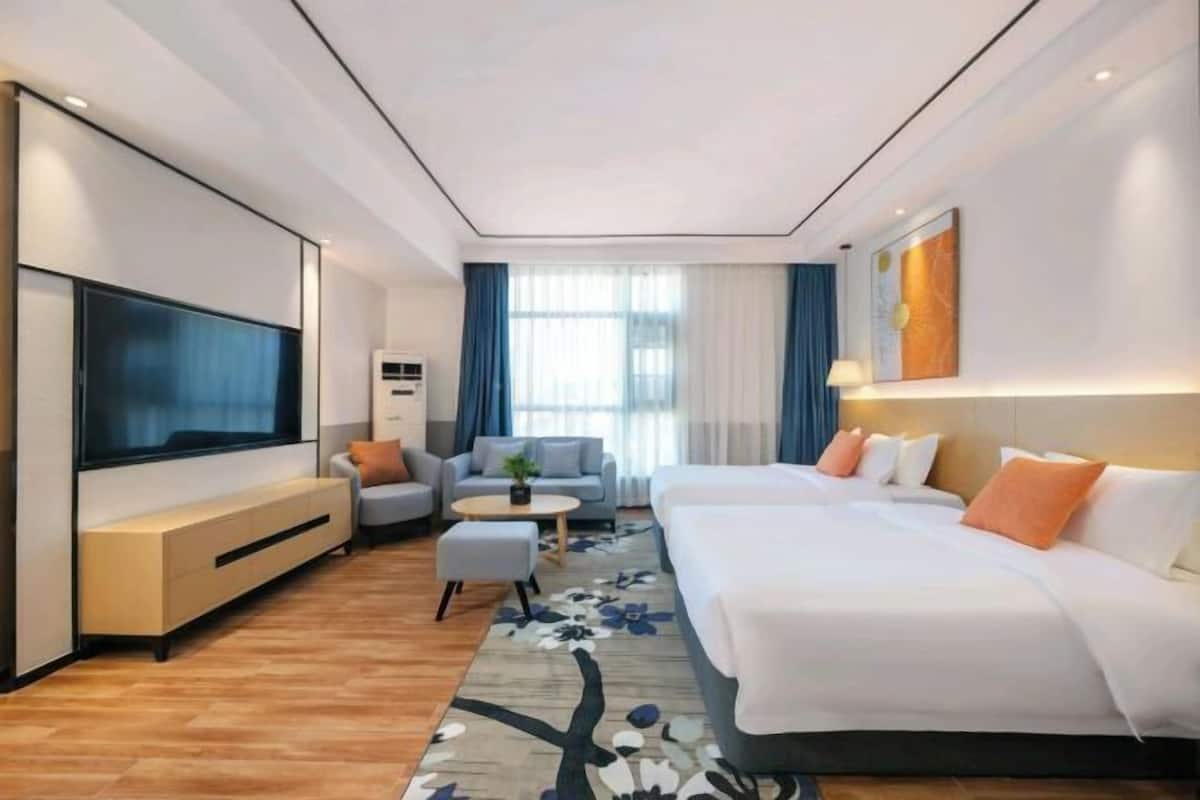A modern hotel room with a large flat-screen TV, a sofa, a bed, a small round table, and a floral rug.