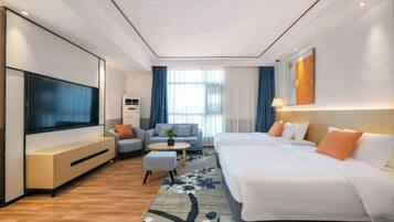 Una habitación de hotel moderna con un televisor de pantalla plana grande, un sofá, una cama, una mesita redonda y una alfombra estampada.