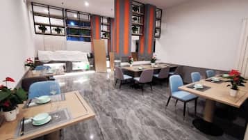 Um espaço de refeições moderno em hotel, com várias mesas e cadeiras, uma cozinha ao fundo e vista para a cidade através de grandes janelas.