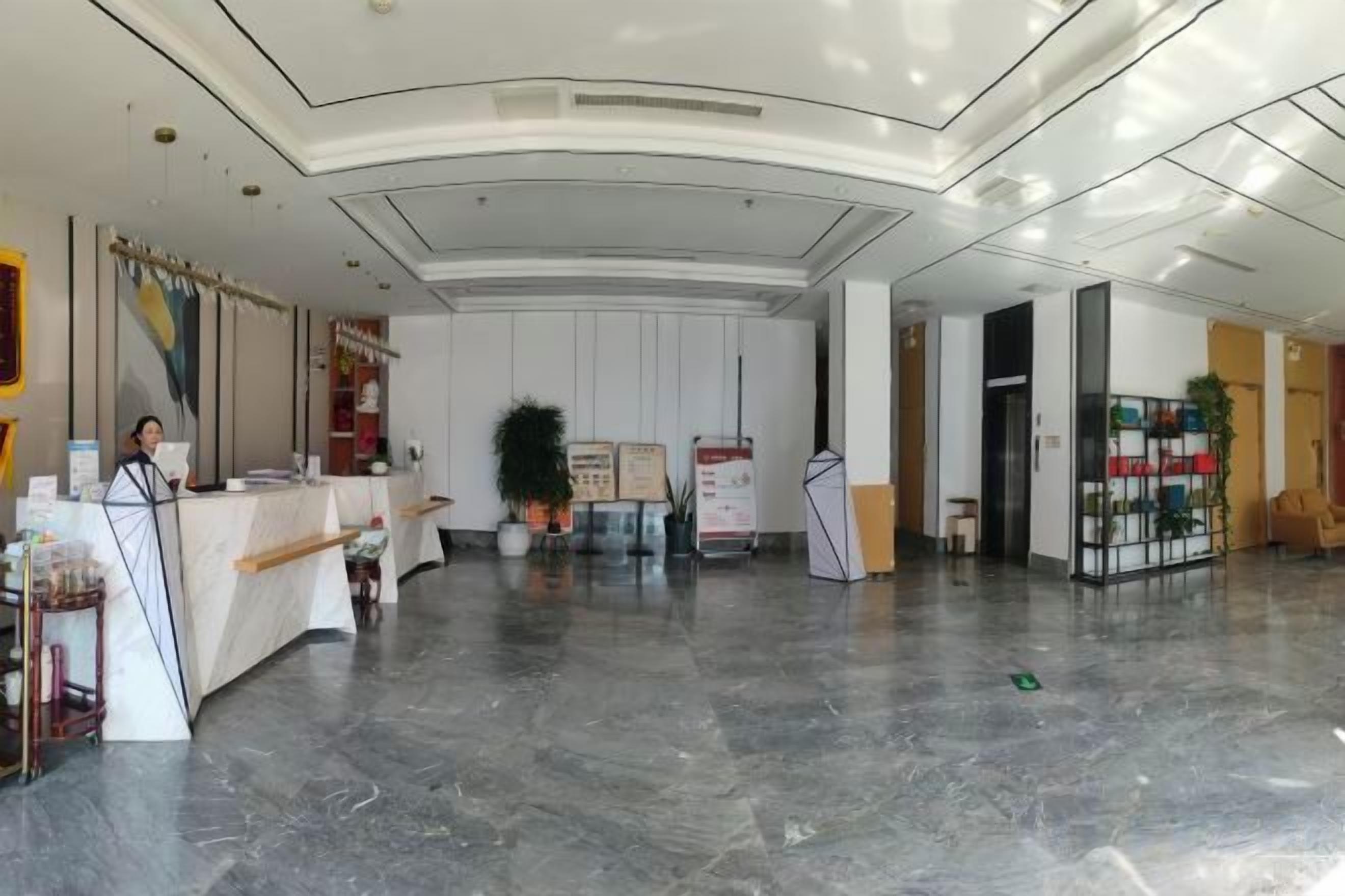 A hotel lobby with a reception desk, a large potted plant, and a seating area with a coffee machine.