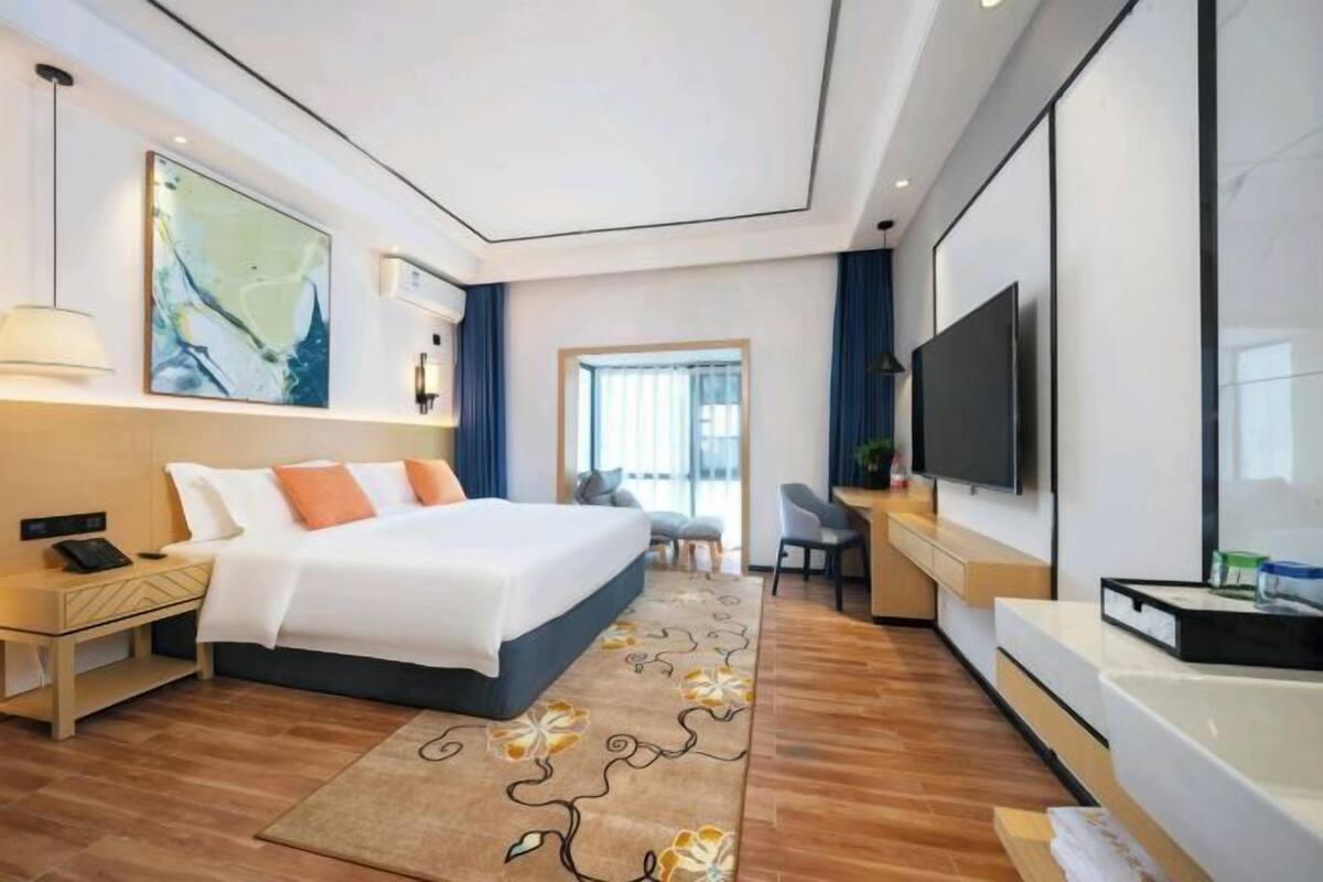 A modern hotel room with a large bed, a desk, a flat-screen TV, and a large window.