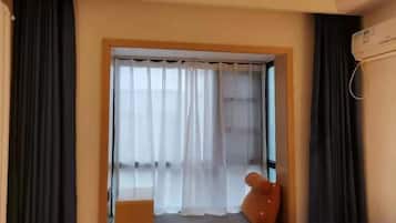 A room with a window, curtains, a small table, and a chair.