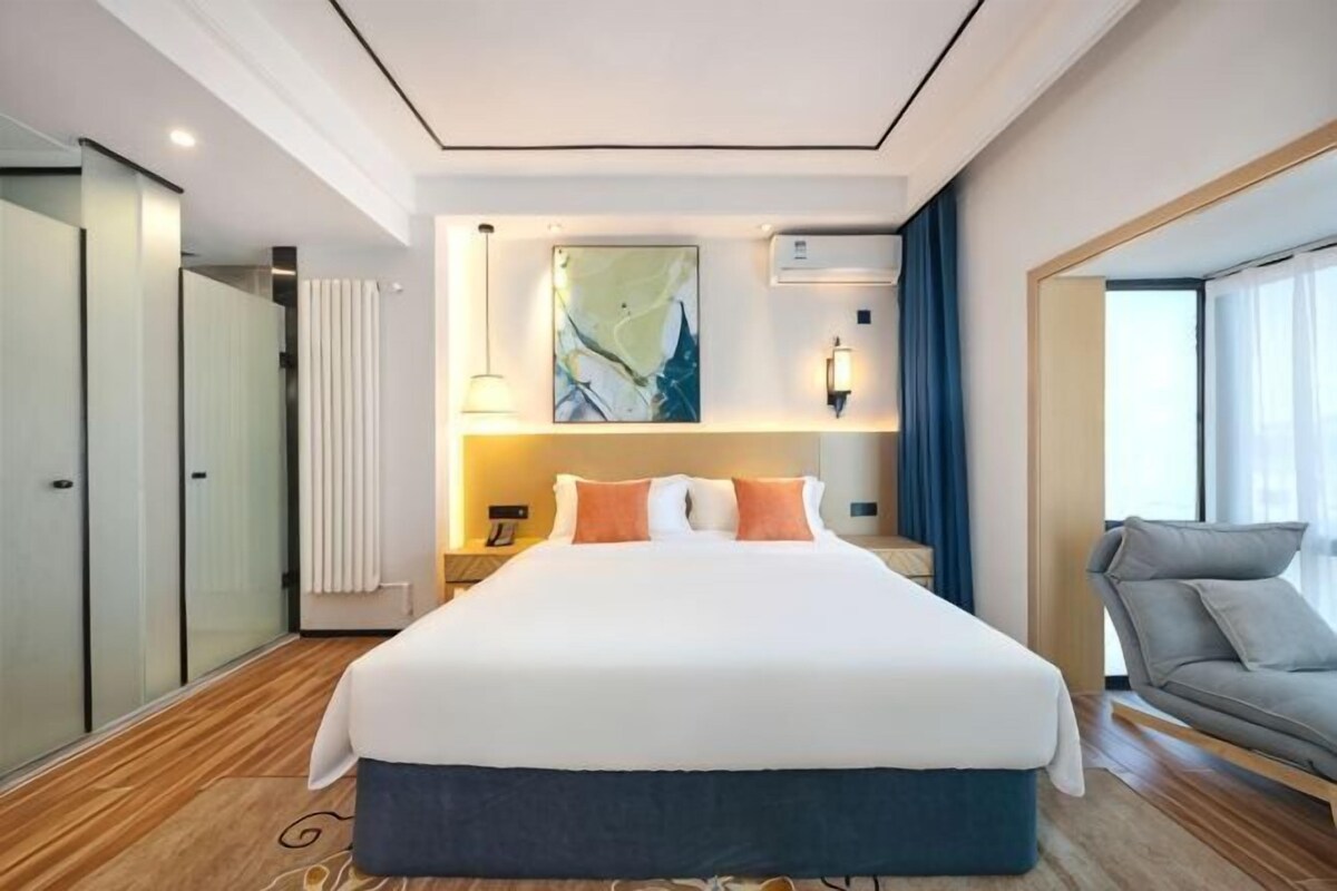 Una camera d'hotel con un letto grande, un divano, un quadro appeso al muro e una finestra.