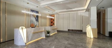 A hotel lobby with marble flooring, a reception desk, and a large abstract painting.