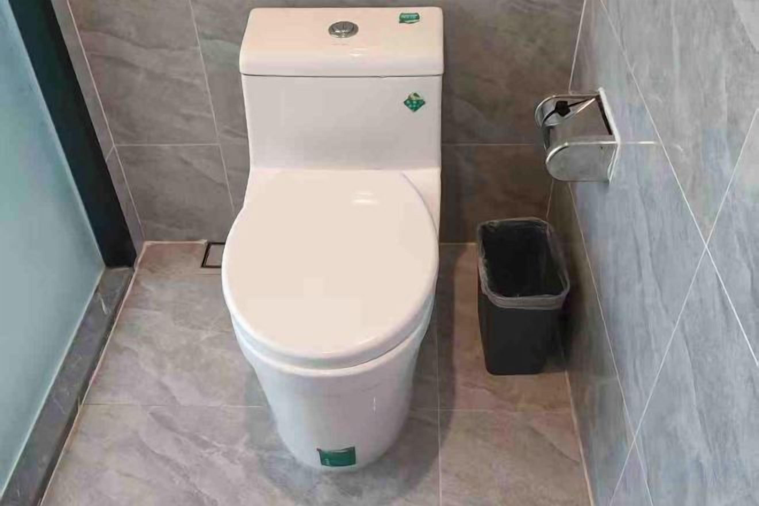 Inodoro con palanca de descarga y un cubo de basura al lado.