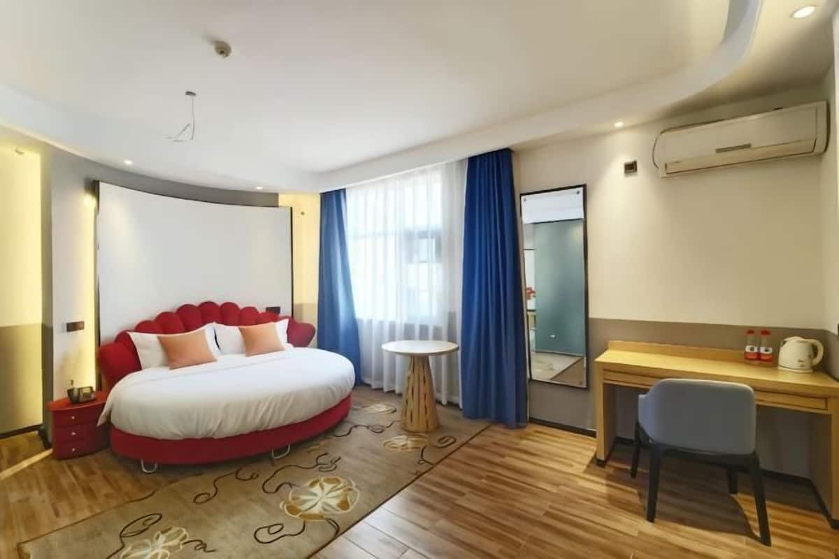 A hotel room with a round bed, a desk, a chair, a small table, and a mirror.