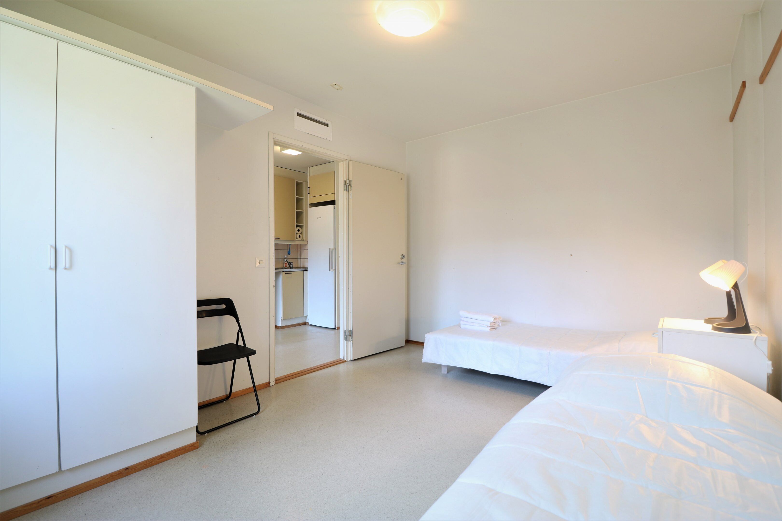 A bedroom with a bed, a nightstand, a chair, and a wardrobe.