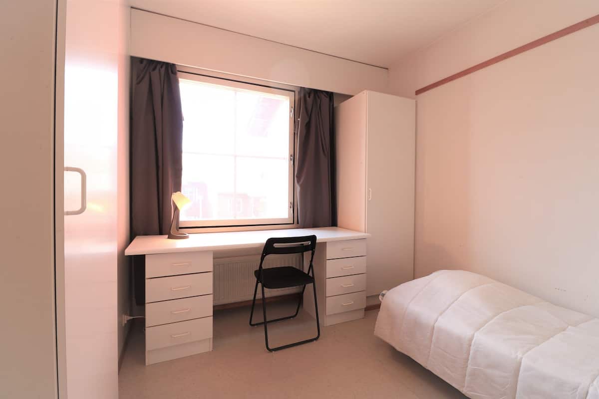 A bedroom with a single bed, a desk with a chair, and a window with curtains.