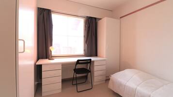 Ein Schlafzimmer mit einem Einzelbett, einem Schreibtisch mit Stuhl und einem Fenster mit Vorhängen.