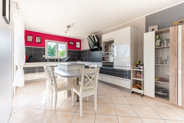 Una cocina moderna con comedor, que incluye una isla grande, sillas blancas y una ventana con vistas a follaje.