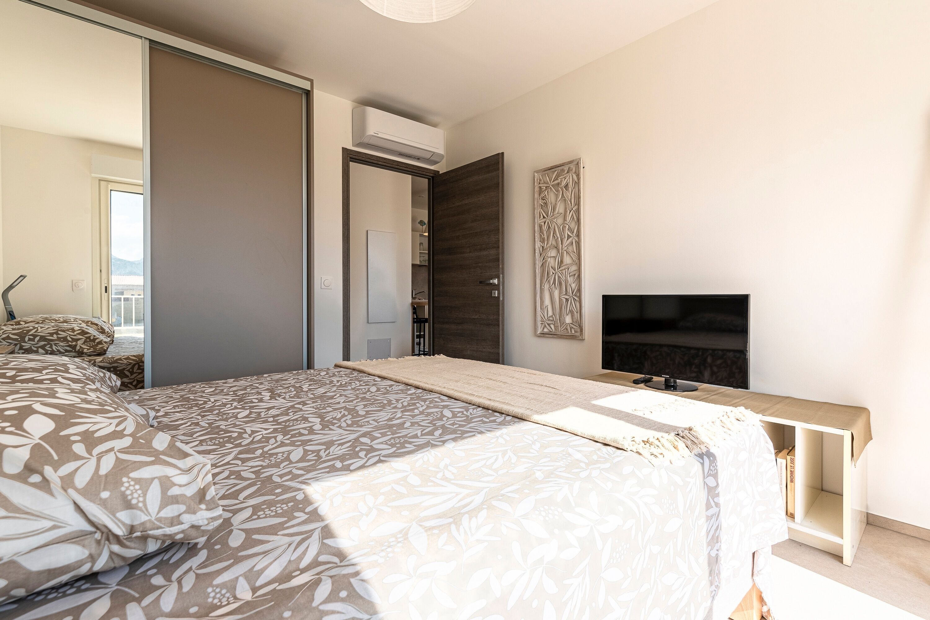 Une chambre moderne avec un grand lit, une télévision et une porte coulissante donnant sur un balcon.