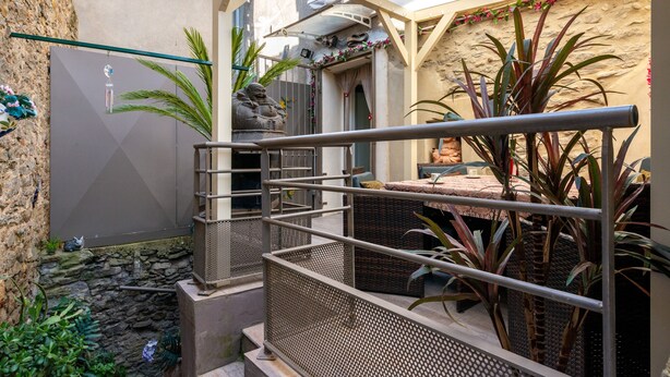 A covered outdoor area with a metal railing, wicker furniture, and potted plants.